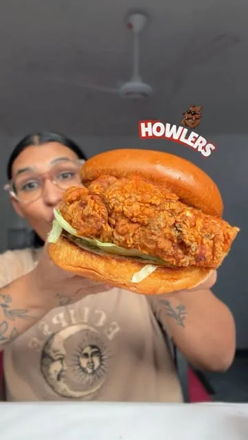 Hands holding a loaded HOWLERS chicken burger